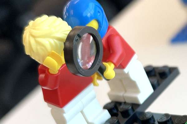 One LEGO minifig holding a magnifying glass up to another minifig.